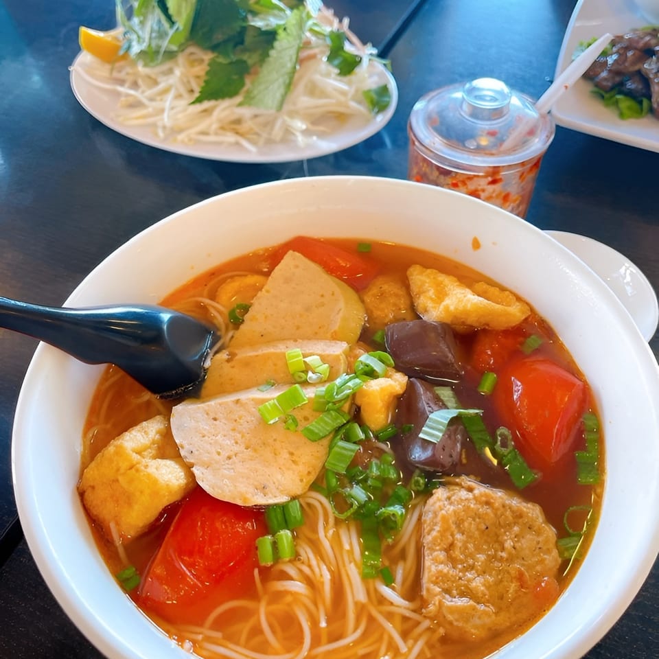 A bowl of Vietnamese bun rieu with noodles, pork, tofu, tomatoes, and green onions.