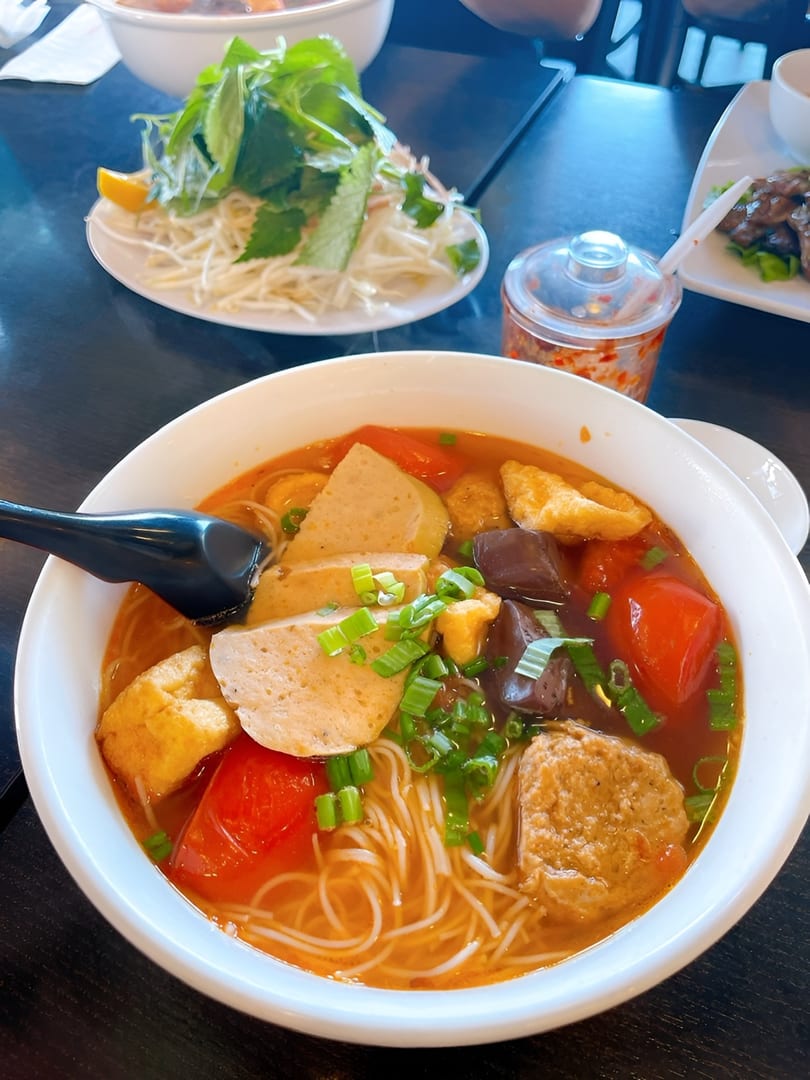 A bowl of Vietnamese bun rieu with noodles, pork, tofu, tomatoes, and green onions.
