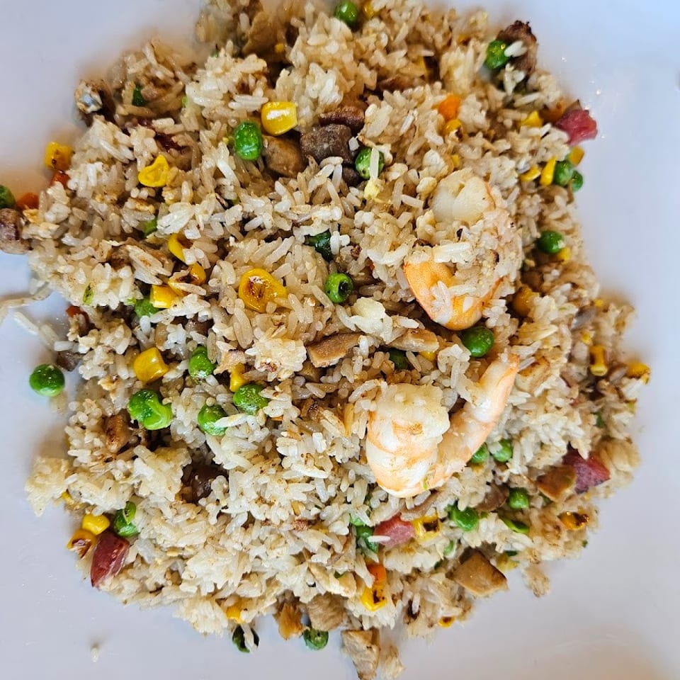 Close-up of fried rice with shrimp, peas, corn, and meat on a white plate.