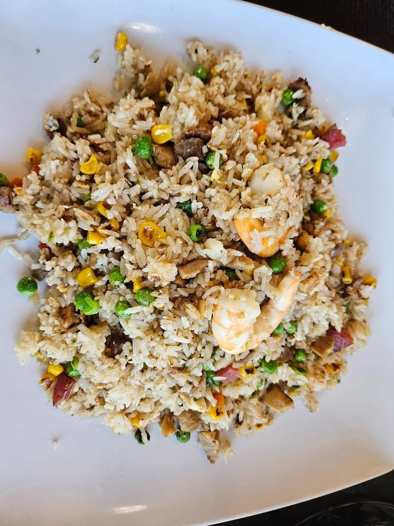 Close-up of fried rice with shrimp, peas, corn, and meat on a white plate.